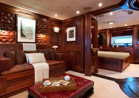 A leather sofa and a coffee tray sit in the foreground of a luxurious wood-paneled room, with a glimpse of a bedroom in the background.