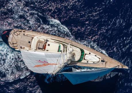 A luxury sailing yacht with white sails glides across a deep blue, choppy ocean.