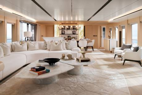 A modern white living area with curved sofas and marble coffee tables sits in the foreground, leading to a dining space and a backlit wall in the background.
