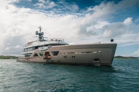 A luxurious superyacht glides through the turquoise waters under a dramatic cloudy sky.