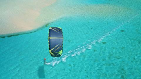 A lone kitesurfer glides across crystal-clear turquoise waters near a sandy shore.