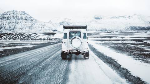 A white off-road vehicle navigates a snow-covered road through a majestic, mountainous winter landscape.
