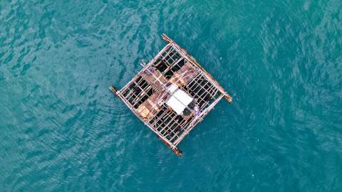A lone figure tends to a rustic bamboo raft floating on the tranquil turquoise waters.