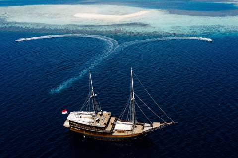 A majestic wooden schooner sails through deep blue waters near a pristine sandbar.