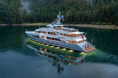 A luxurious yacht glides through serene, tree-lined waters, its interior lights reflecting on the calm surface.