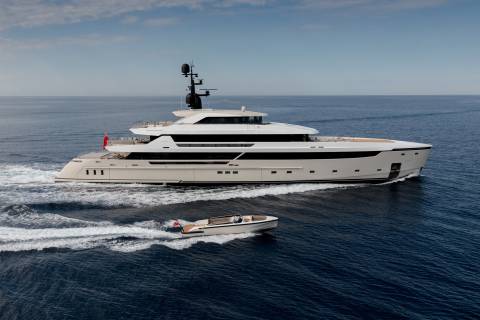 A sleek superyacht cruises through the deep blue sea, trailed by a smaller tender boat.