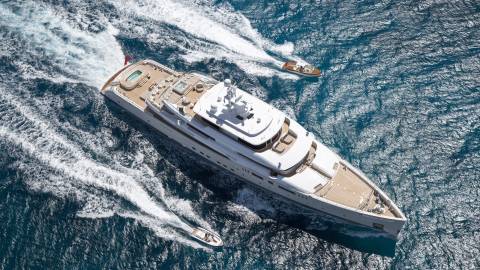 A luxurious superyacht cruises through the deep blue ocean, trailed by two smaller boats.