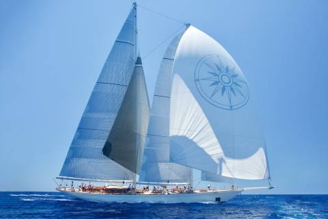 A majestic white sailboat with a compass rose on its sail glides across the deep blue ocean under a clear sky.