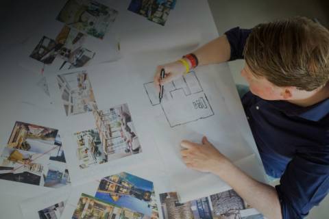 An interior designer sketches a floor plan surrounded by inspirational images of various architectural styles.