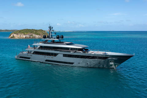 A sleek, modern superyacht glides through the turquoise waters of a tropical bay.