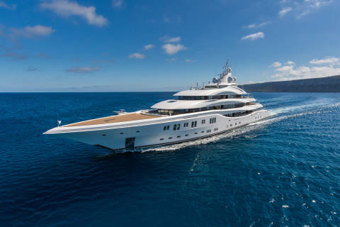 A majestic white superyacht cruises through the deep blue ocean under a sky dotted with fluffy white clouds.