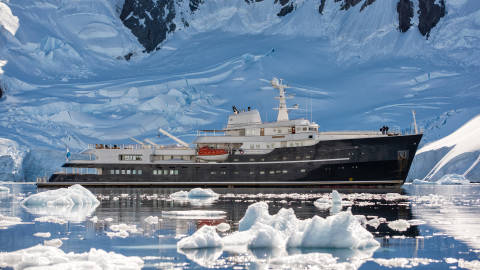 A luxury yacht navigates through a serene Antarctic landscape dotted with icebergs and towering glaciers.