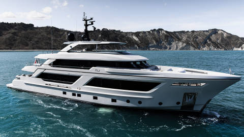 A sleek white yacht glides through the turquoise waters with rugged, tree-covered hills in the background.