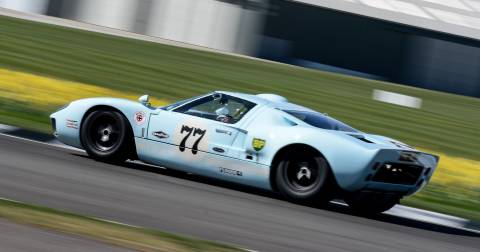 A light blue Ford GT40 races down the track, its number 77 prominently displayed.