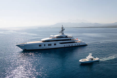 A luxurious superyacht glides across the sparkling blue ocean, accompanied by a smaller tender boat.