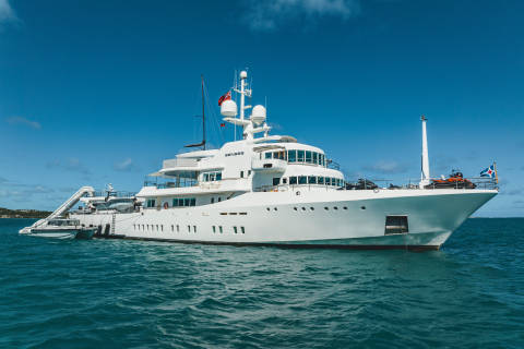 A luxurious white superyacht named Senses cruises on turquoise waters under a clear blue sky.