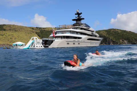 A couple enjoys a thrilling ride on jet skis in the turquoise waters near a luxurious yacht and inflatable water park.