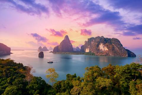 A boat glides across serene waters amidst dramatic limestone karsts under a vibrant sunset sky.