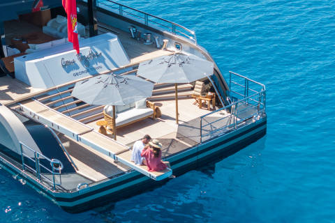 A couple relaxes on the deck of a luxury yacht, enjoying the crystal-clear blue waters.