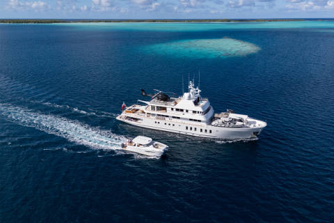A luxurious superyacht and its tender cruise through the crystal-clear turquoise waters of a tropical atoll.