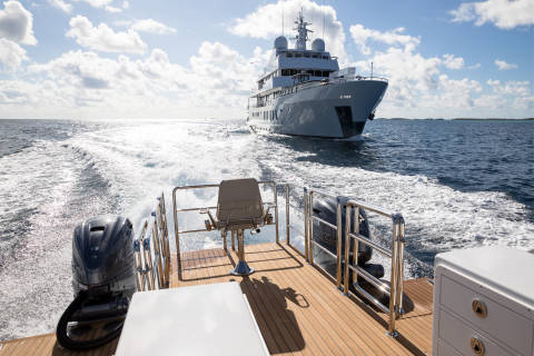 A sleek yacht cruises through the ocean, leaving a frothy wake behind a smaller chase boat.