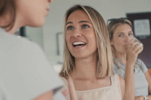 The image shows a group of three young women, one of whom is laughing and smiling brightly while the other two appear to be engaged in conversation.