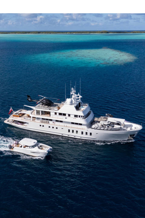 A luxurious superyacht with a helicopter on deck sails through turquoise waters near a tropical island.