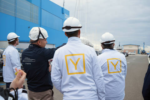 A group of workers wearing hard hats and safety vests with the letter "Y" printed on the back, standing in front of a large blue building.
