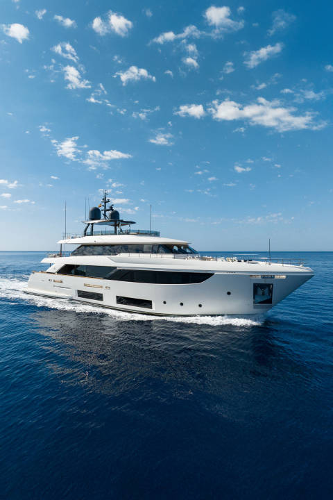 A sleek white yacht cruises through deep blue water under a bright sky with scattered clouds.
