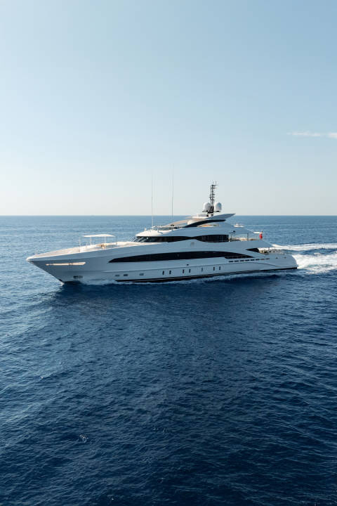 A large white yacht cruises through deep blue water under a clear sky.