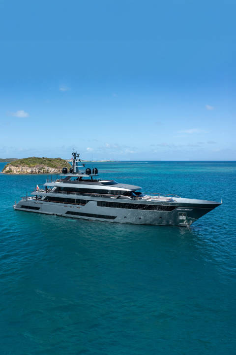 A sleek, modern yacht floats on calm, turquoise waters with a lush, green island in the distance under a clear blue sky.