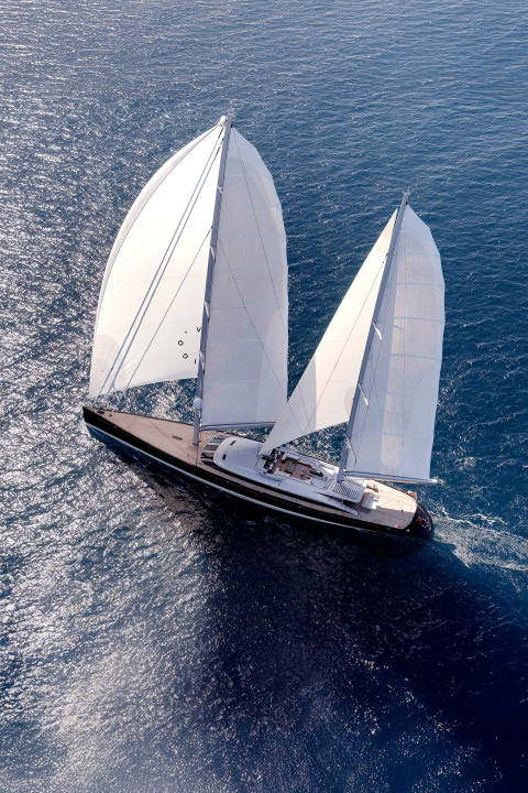 A large sailboat with full white sails glides across a deep blue ocean.