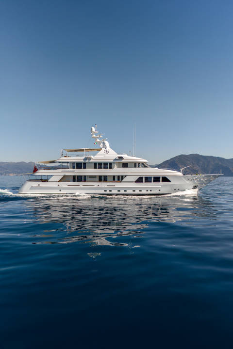 A large white yacht cruises on calm blue water with a hazy green coastline in the background under a clear sky.