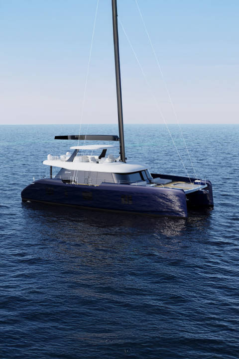 A sleek, dark blue catamaran with a tall mast floats on calm, deep blue water under a clear sky.