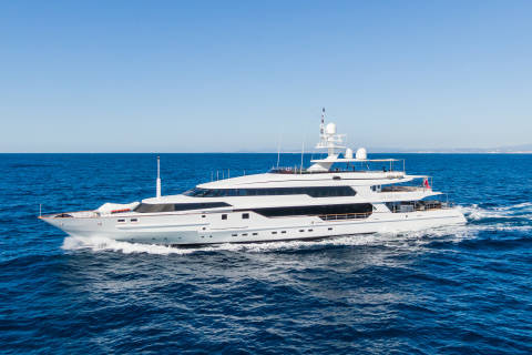 A large white yacht cruises through the deep blue ocean under a clear sky.