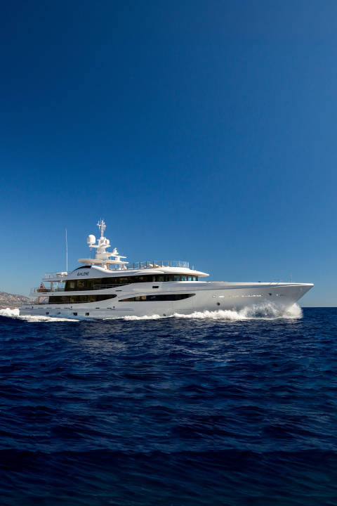 A large white yacht cruises through deep blue water with a hazy coastline in the background under a clear blue sky.