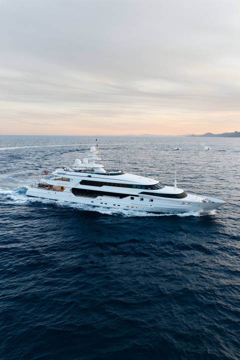 A large white yacht cruises through deep blue water, with a soft, hazy sky and distant landmass in the background.