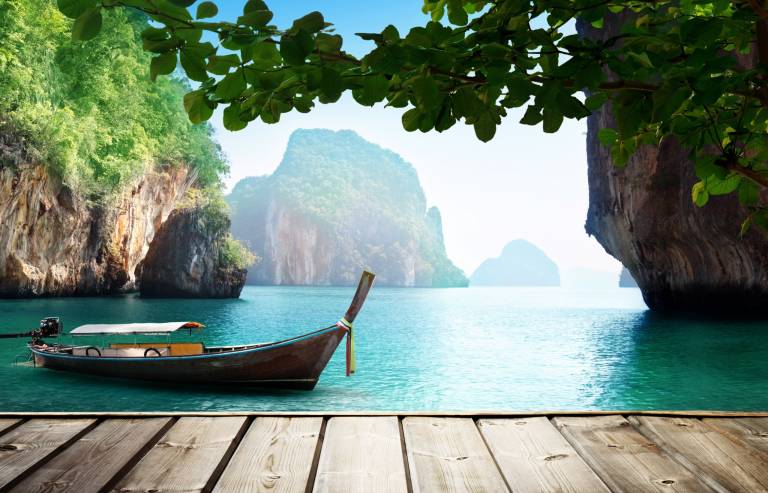 A traditional longtail boat floats serenely in the turquoise waters of a tropical bay, framed by lush green foliage and dramatic limestone cliffs.