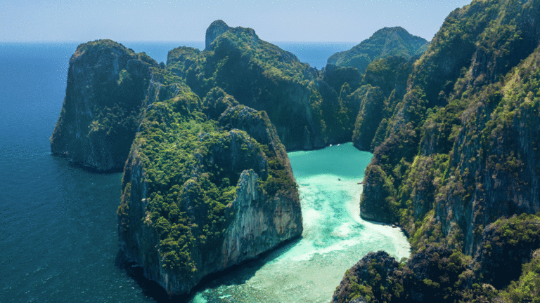 Lush green cliffs plunge into the crystal-clear turquoise waters of a secluded tropical bay.