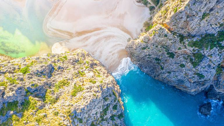 A breathtaking aerial view captures the dramatic convergence of turquoise waters and rugged cliffs at a secluded coastal cove.