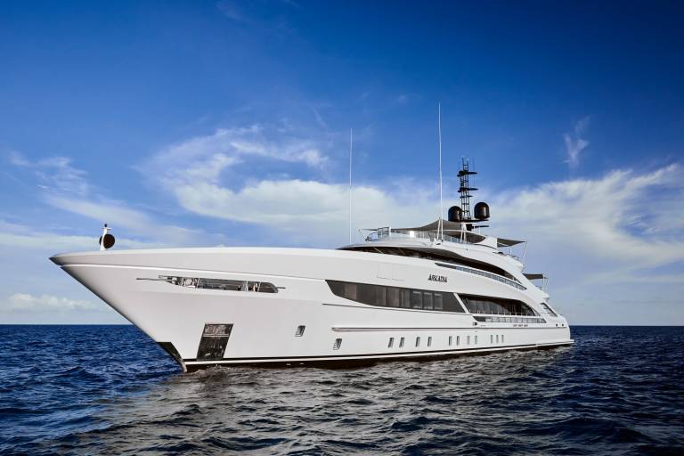 The gleaming white superyacht Arkadia glides serenely across the deep blue ocean under a sky dotted with wispy clouds.