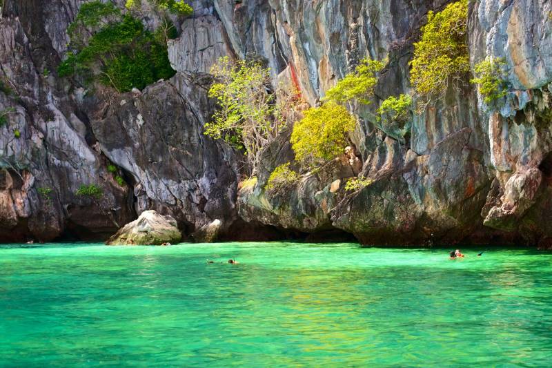 Snorkelers explore the crystal-clear turquoise waters surrounding dramatic limestone cliffs adorned with lush greenery.