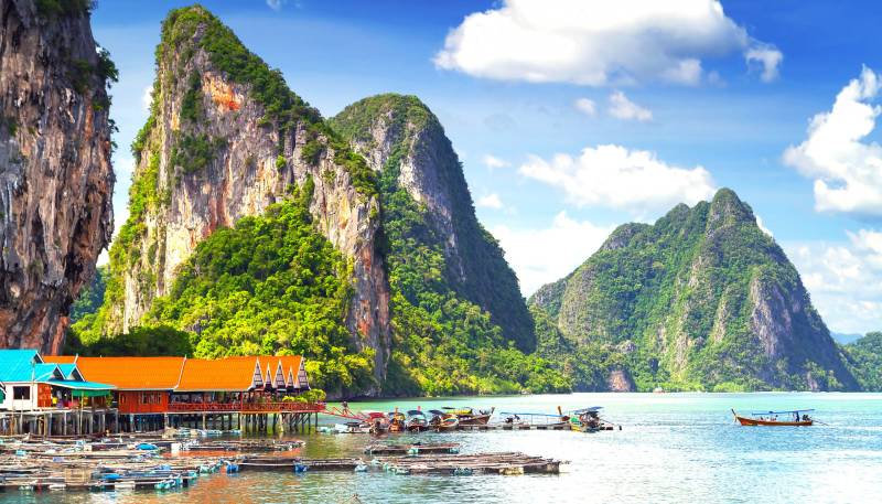 Floating villages nestle at the base of dramatic limestone karsts under a vibrant blue sky.