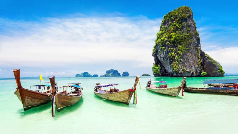 Traditional longtail boats float in the crystal-clear turquoise waters of a Thai island paradise.