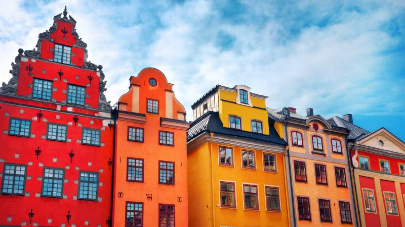 Colorful historic buildings with intricate facades line a street under a bright blue sky with scattered clouds.