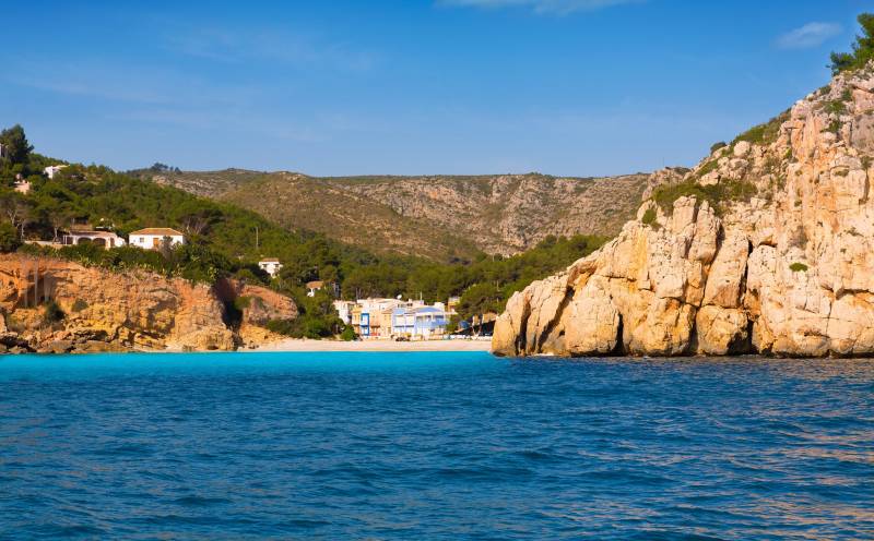 Brightly colored houses line a pebble beach nestled between dramatic cliffs and the azure Mediterranean Sea.
