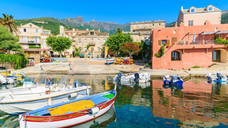 Colorful boats bob in the clear turquoise water of a charming coastal village nestled against a backdrop of verdant mountains.