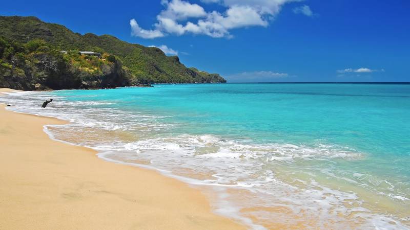 Turquoise waves gently kiss the golden sand of this secluded tropical beach beneath lush green hills.