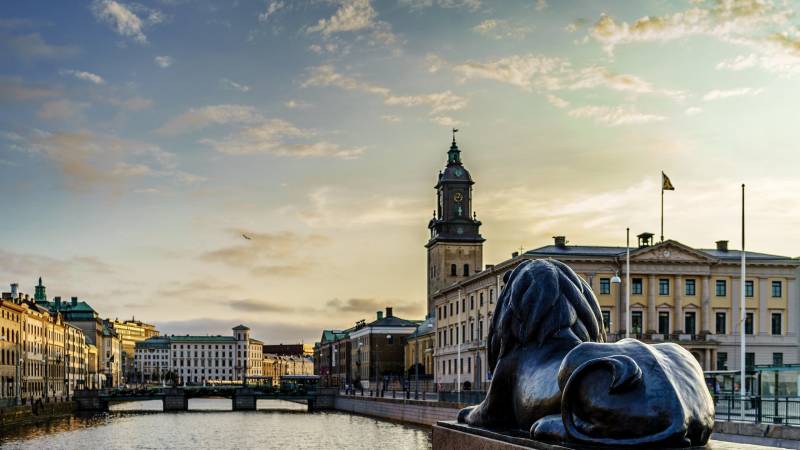 A bronze lion statue overlooks a canal lined with historic buildings and a clock tower under a dramatic sky.