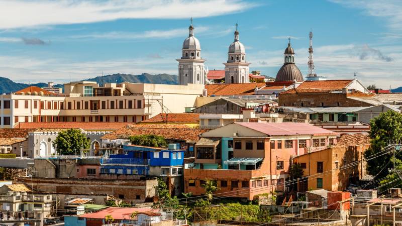 The vibrant cityscape is crowned by the iconic domes of a grand cathedral under a bright blue sky.